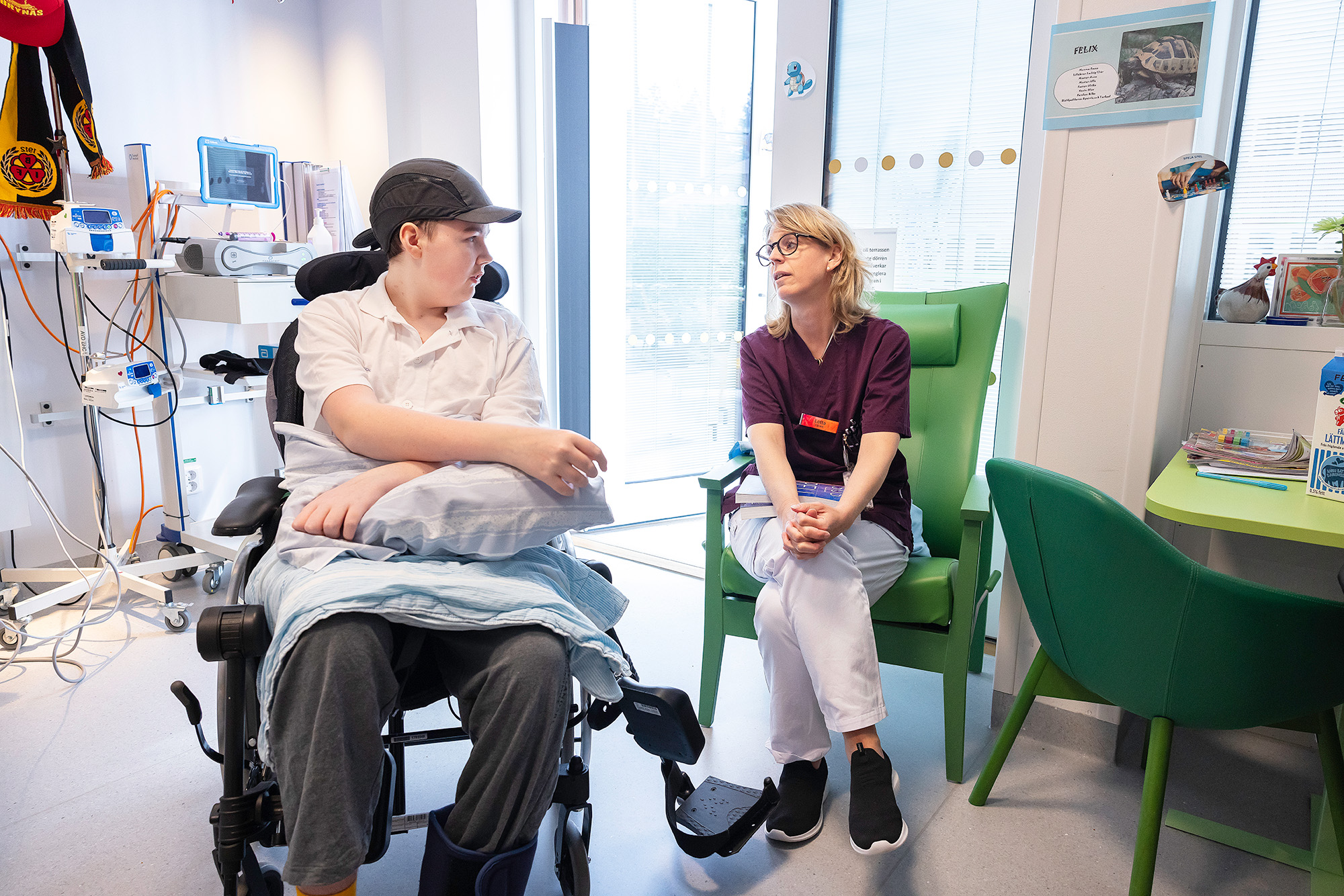 A teenager in a wheelchair talking to the hospitals teacher.