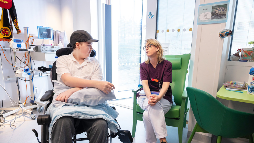 A teenager in a wheelchair talking to the hospitals teacher.