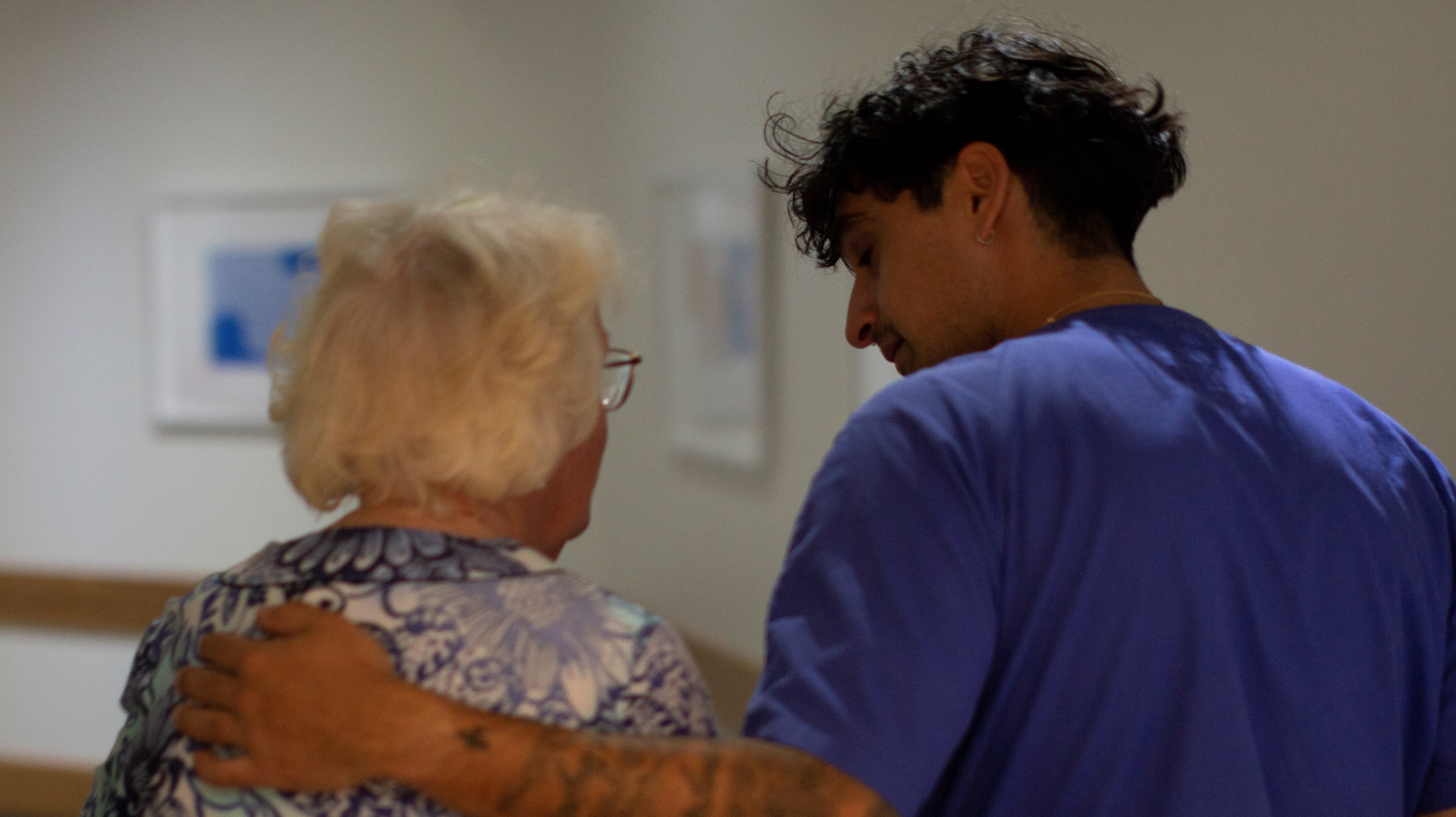 En manlig vårdpersonal leder en äldre kvinnlig patient