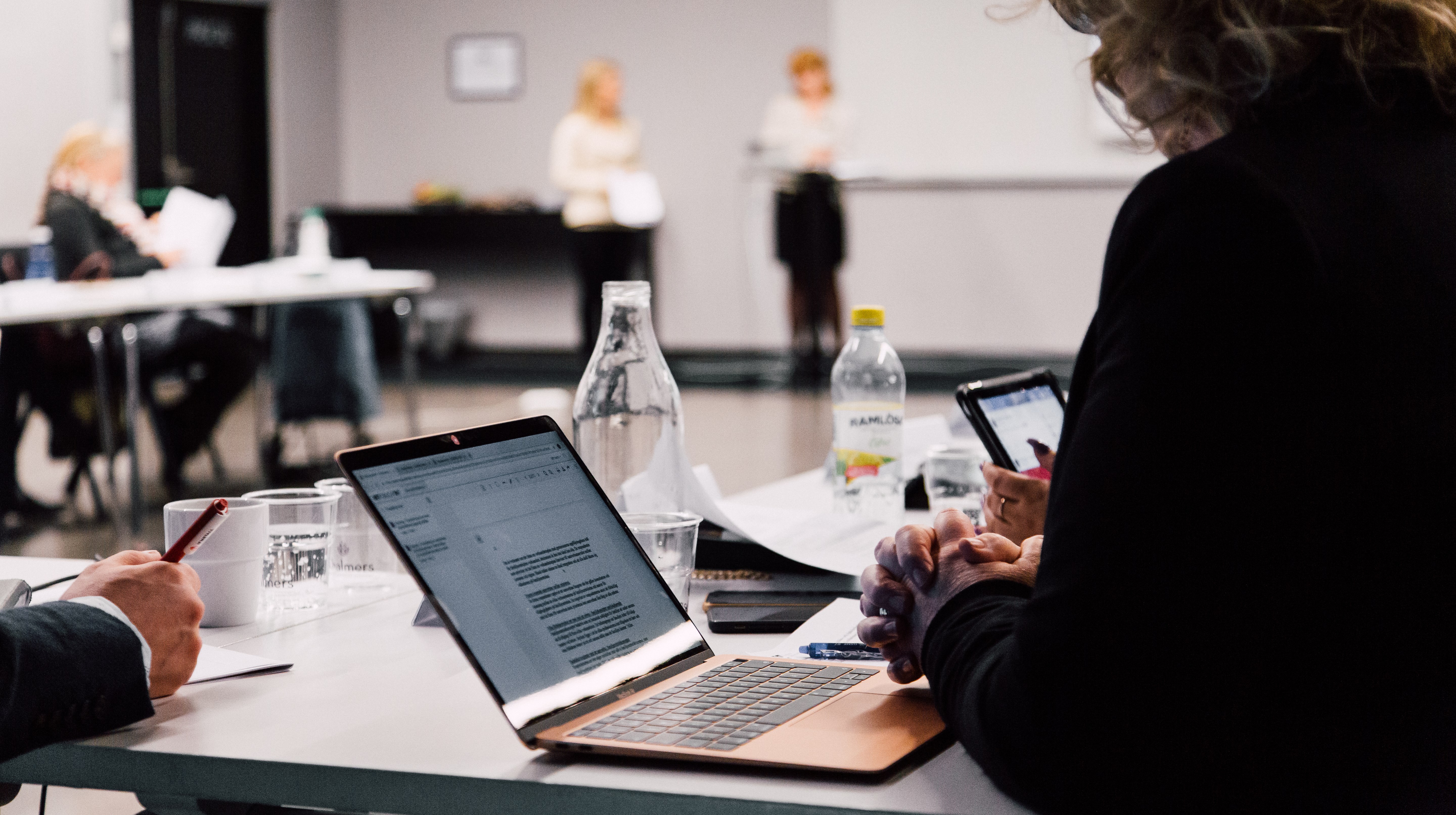 Kvinna sitter vid dator i ett mötesrum under en konferens.