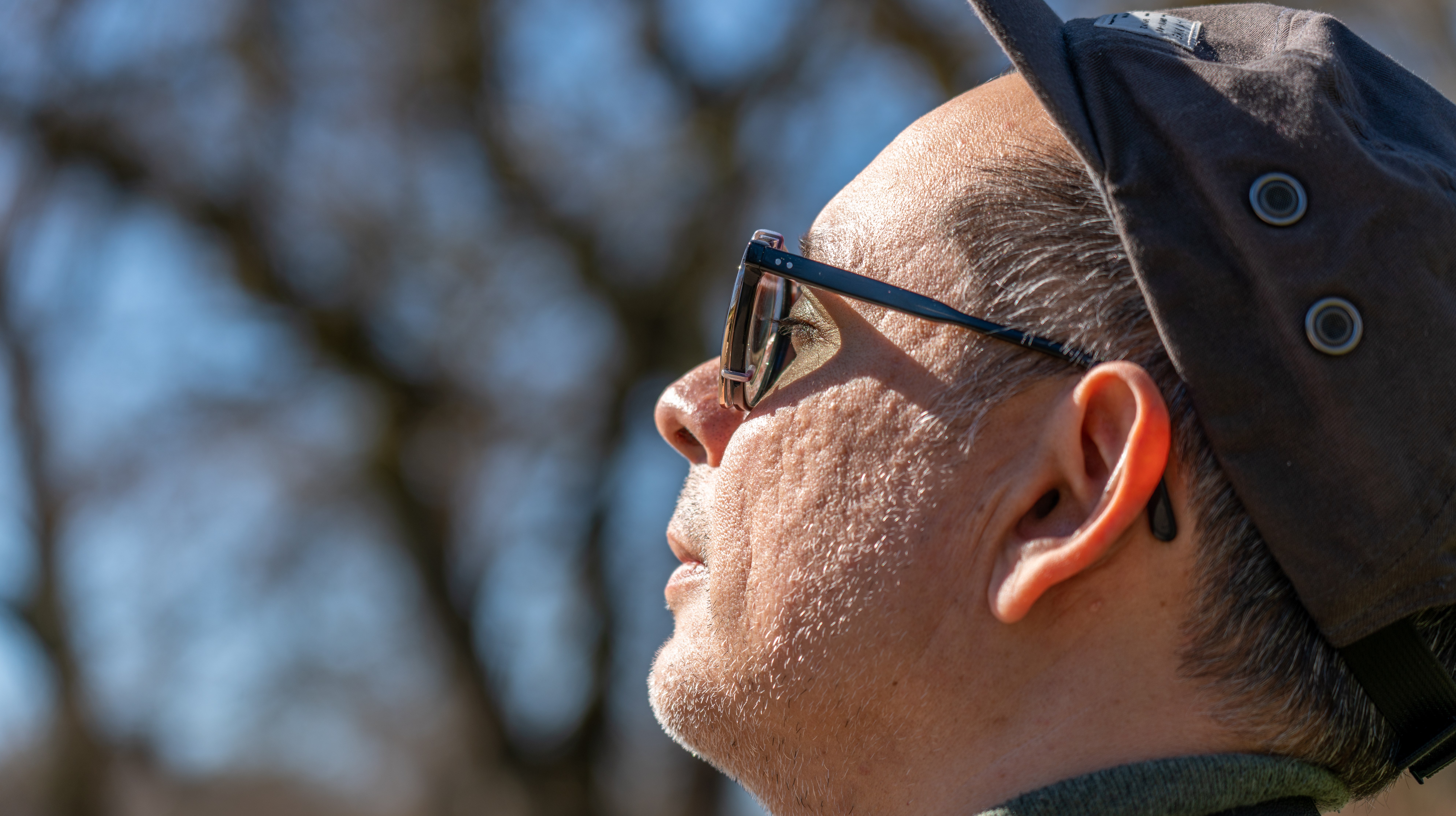 Vuxen person med keps och glasögon vänder ansiktet mot solen och blundar.