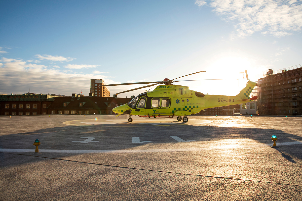 An ambulance helicopter parked on a helipad, the sun setting behind it.