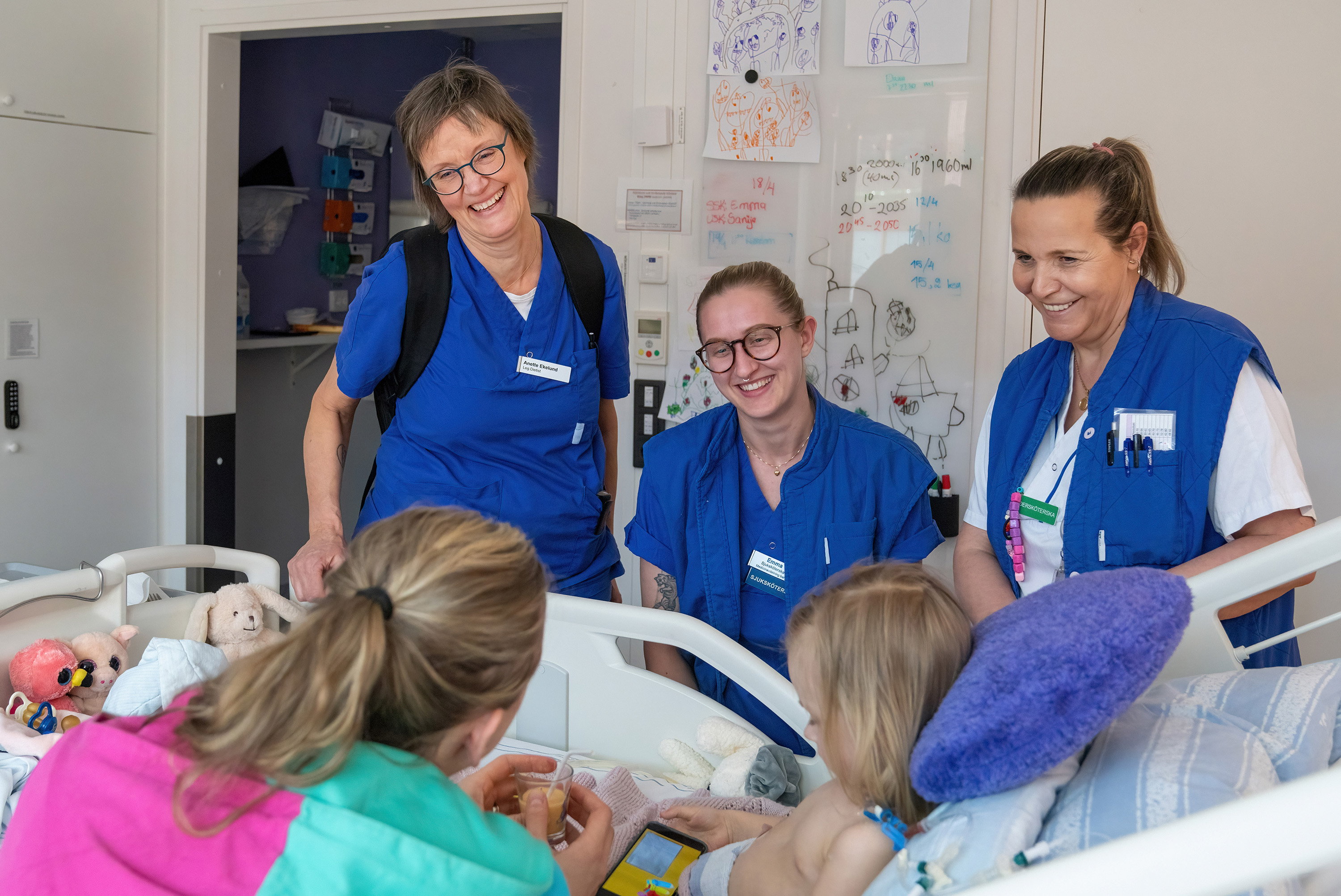 Three nurses with two children in a hospital bed.