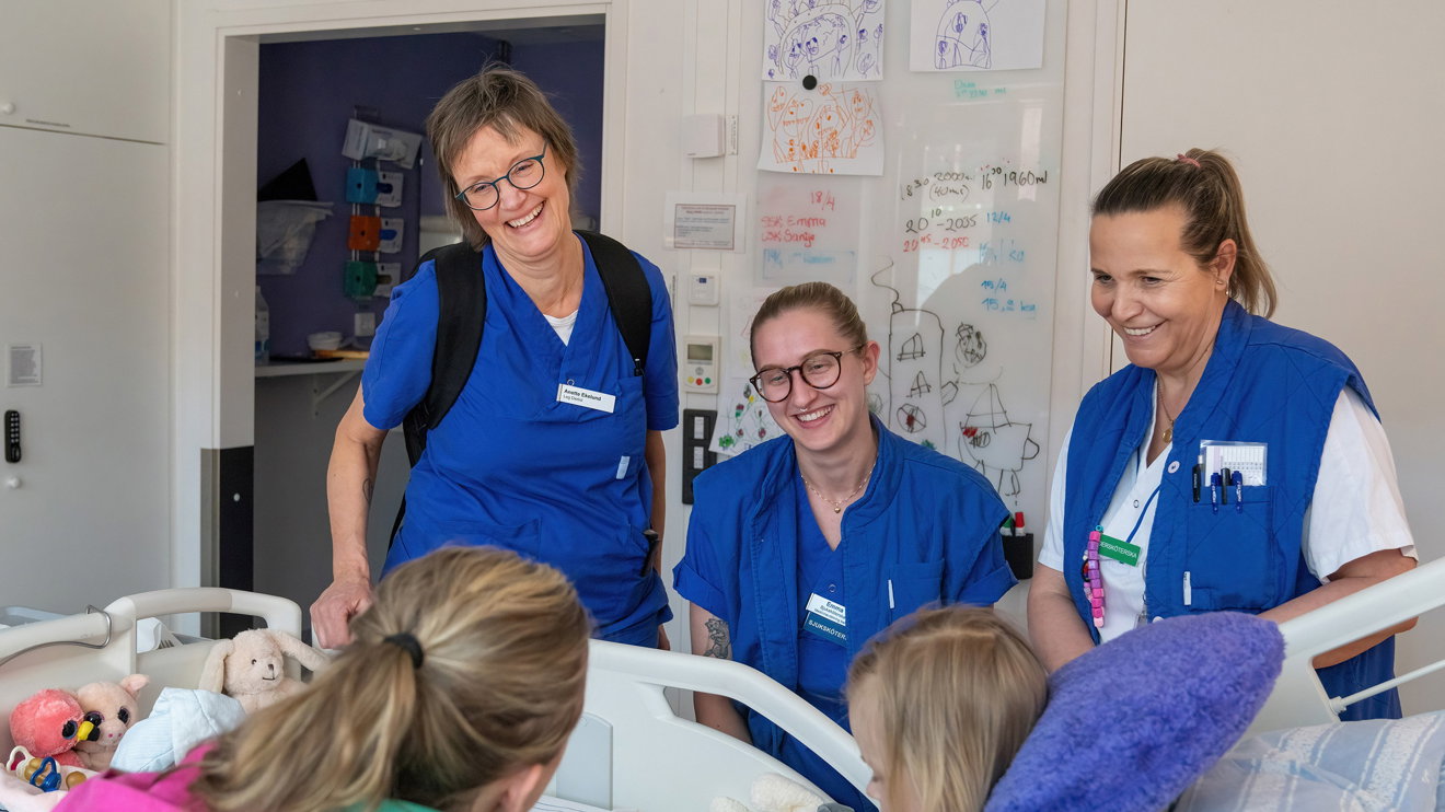Three nurses with two children in a hospital bed.