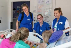 Three nurses with two children in a hospital bed.