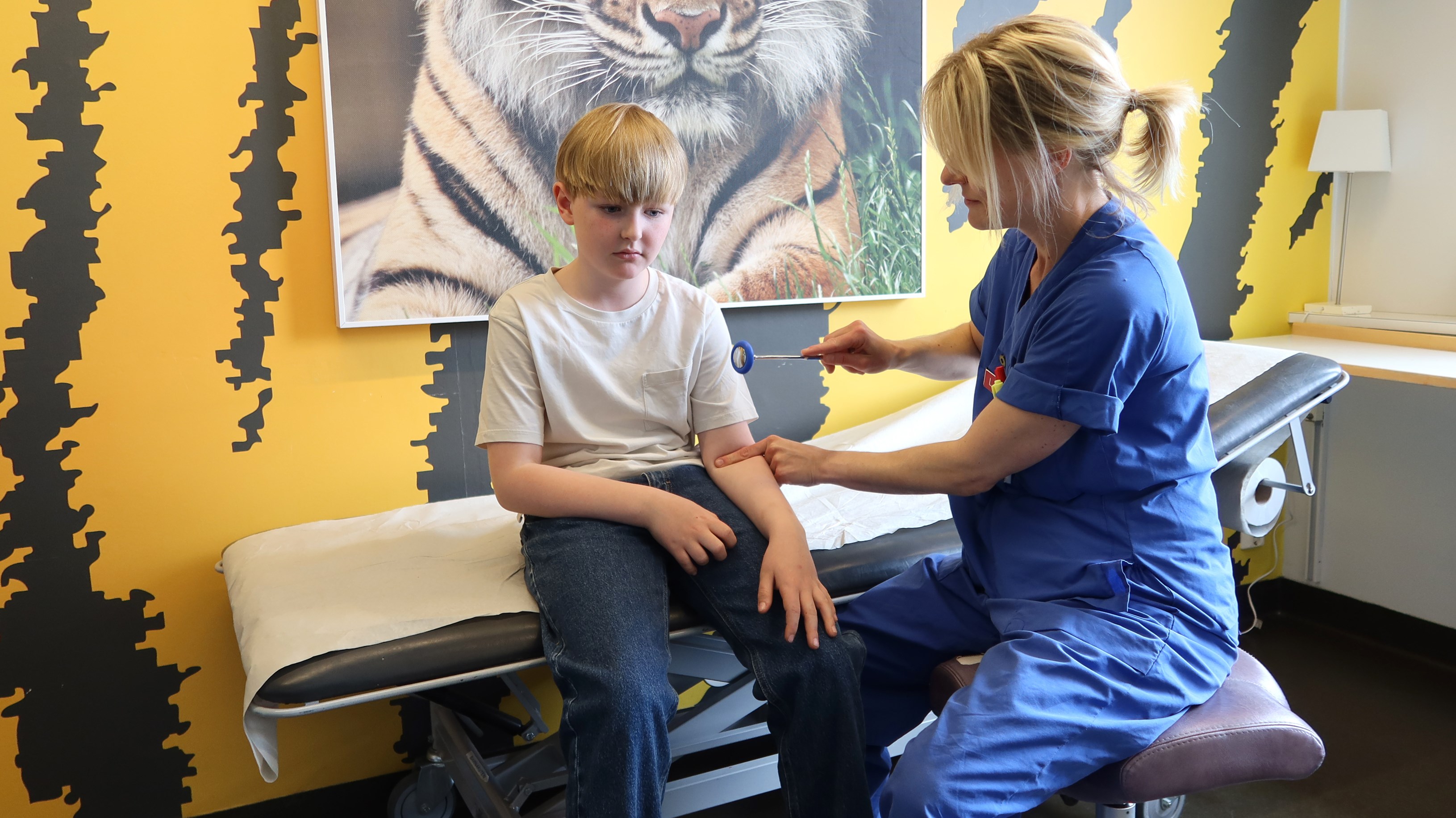 En doktor slår med en liten klubba i armvecket på ett barn