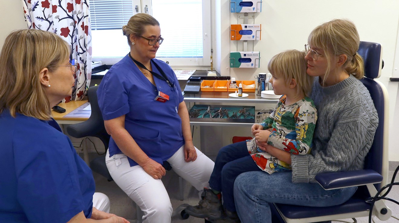 En läkare pratar med ett barn som sitter i mammas knä
