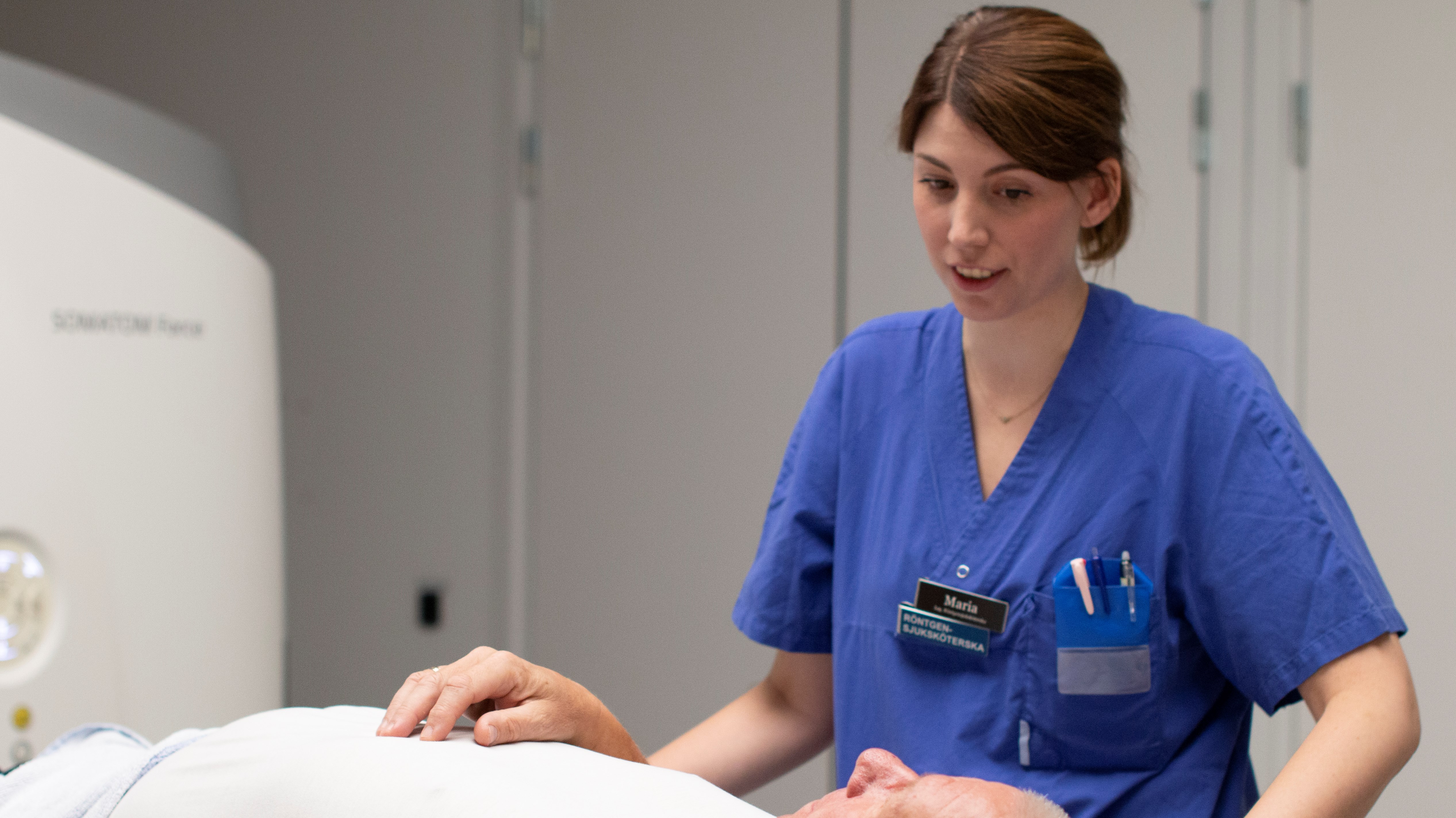 Vårdpersonal pratar med patient som ligger på brits.