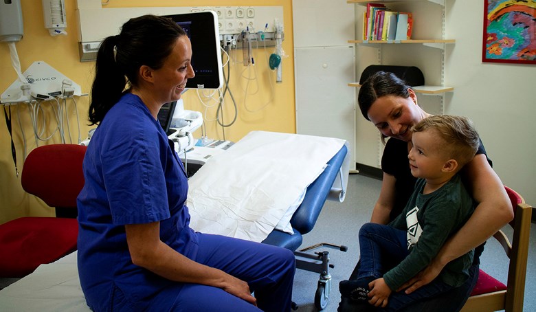 Ett barn i mammas knä pratar med en sjuksköterska.