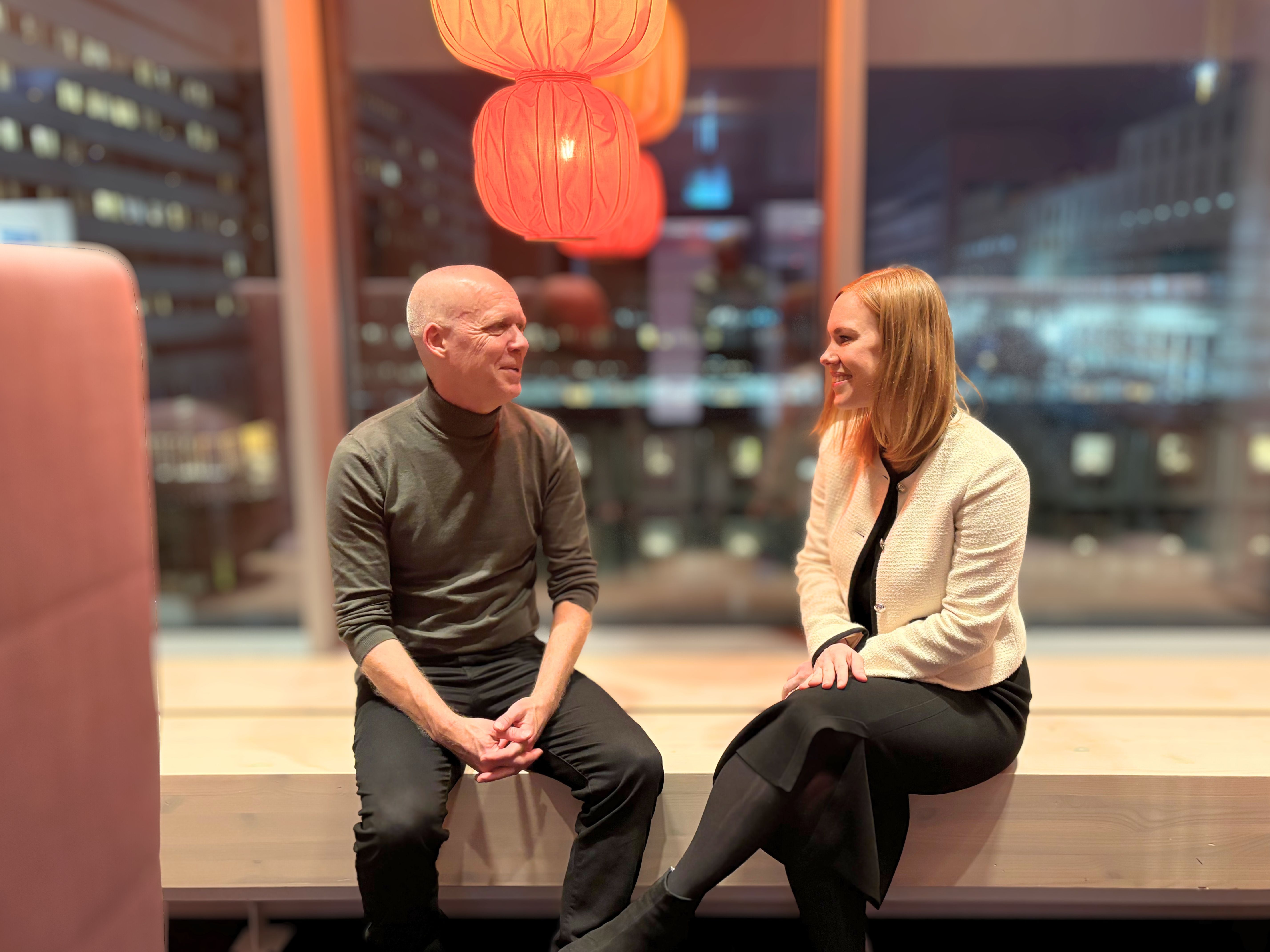 A man and a woman talking on a bench indoors.