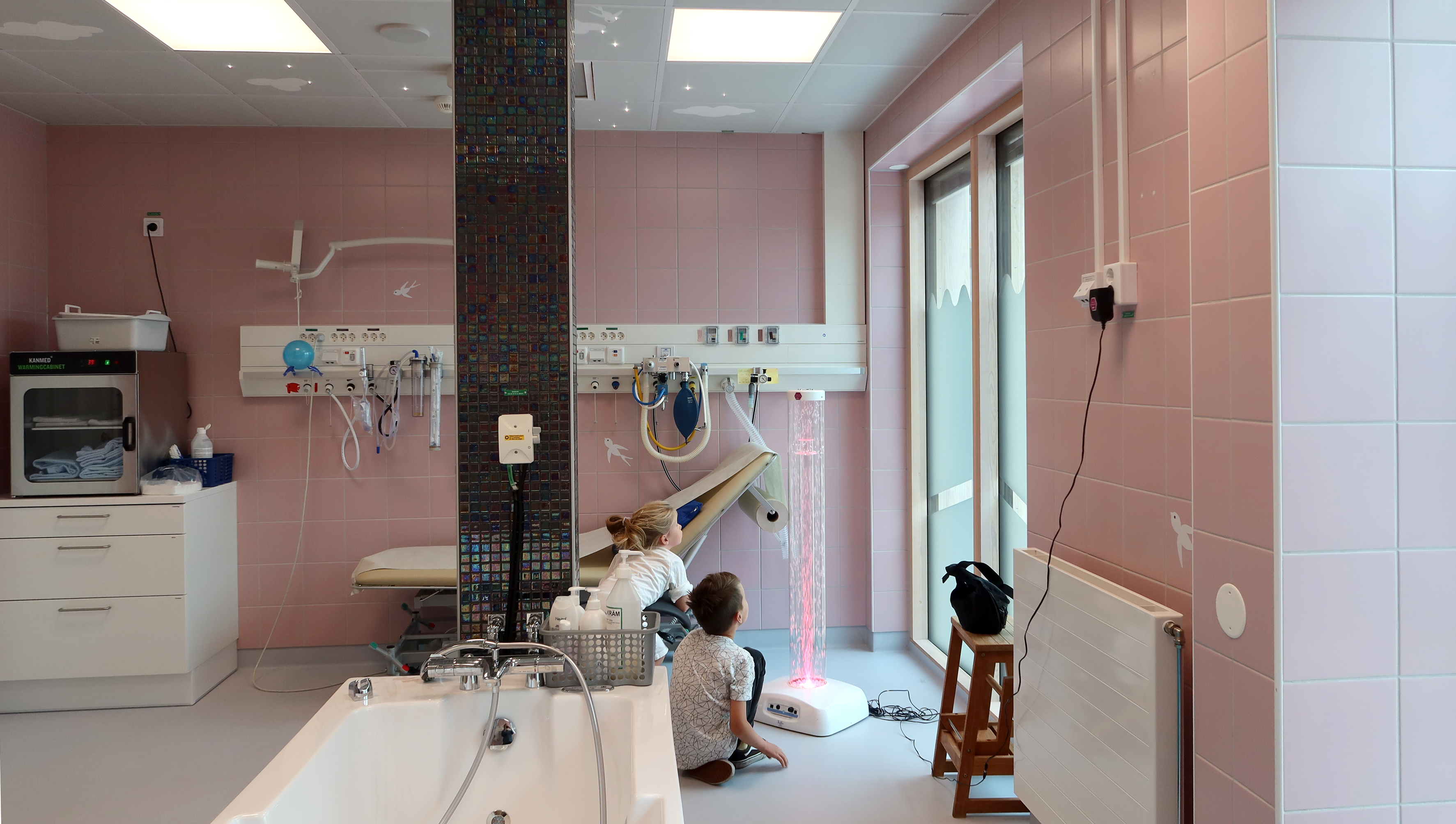 Ett stort badrum. Två barn framför en lampa. 