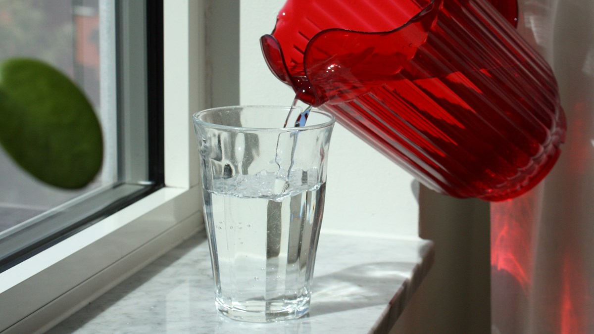 Bild på upphällning av ett glas vatten med en röd tillbringare.