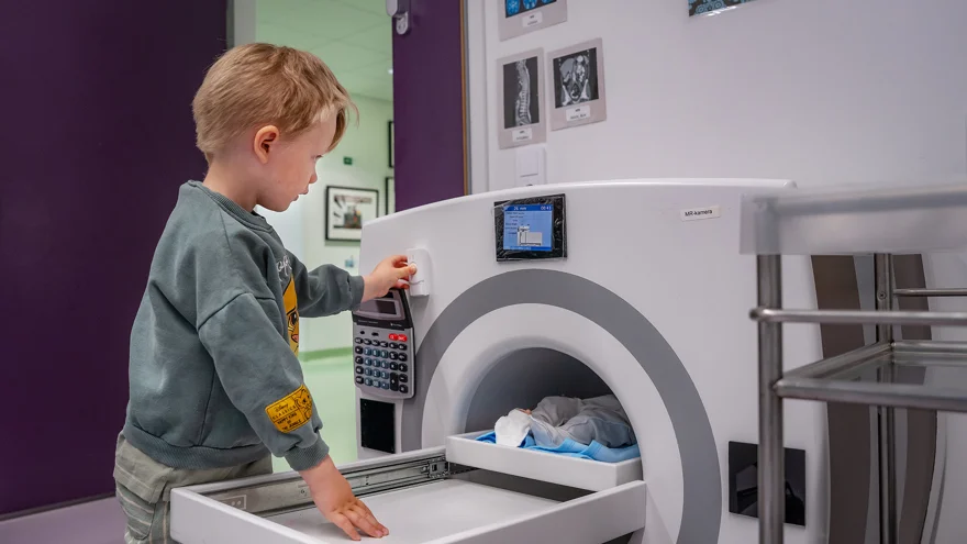 A child playing with a doll in a toy MRI machine.