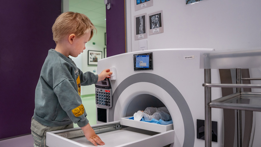 A child playing with a doll in a toy MRI machine.