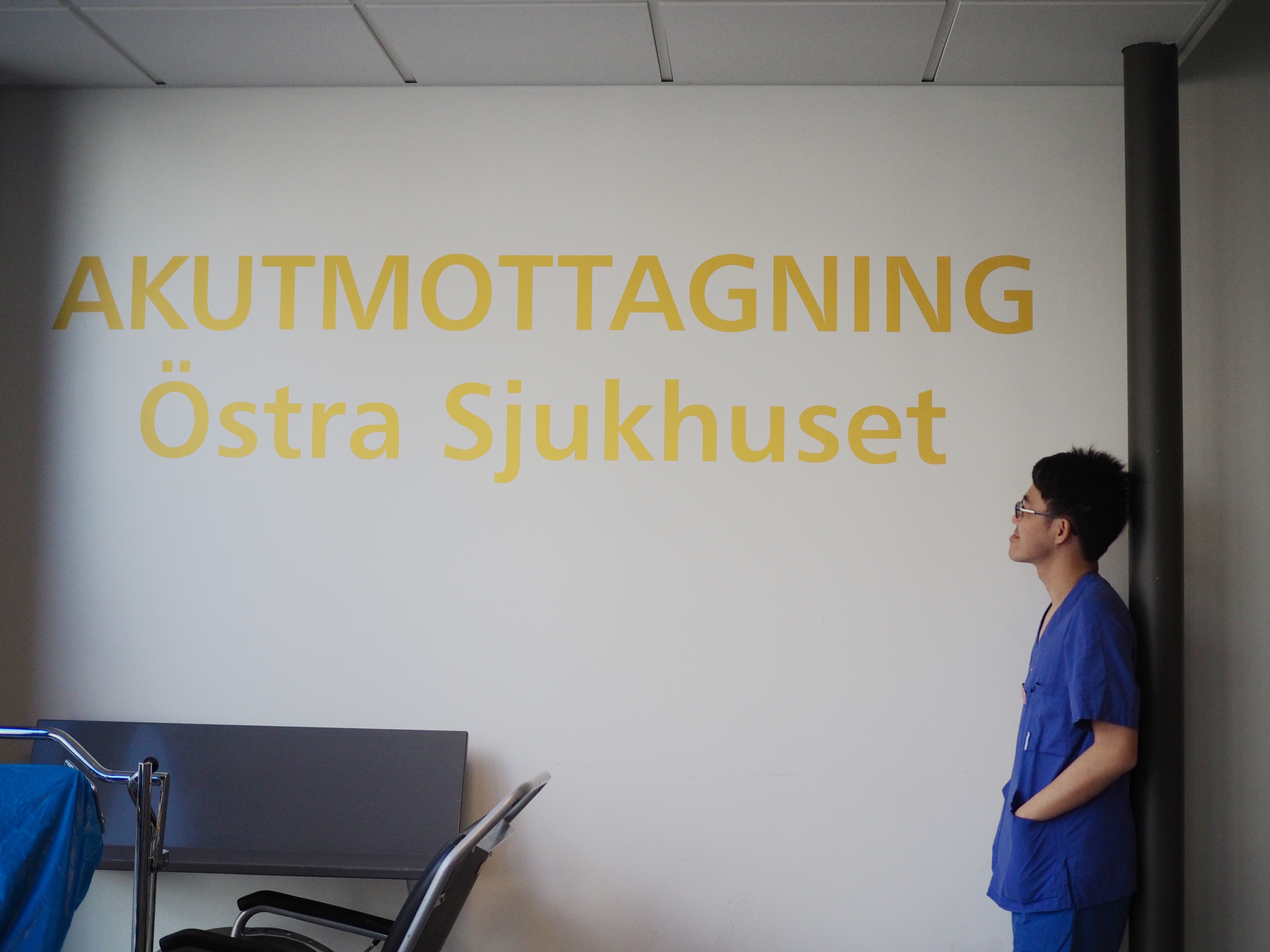 Dr Toon in blue scrubs looking at white wall with yellow letters saying "Emergency department, Östra Hospital"