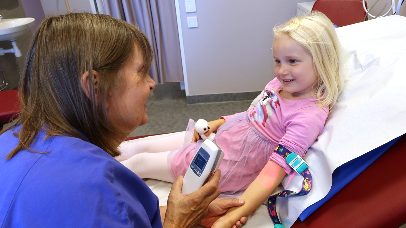 En sköterska lyser med en apparat på ett barns arm