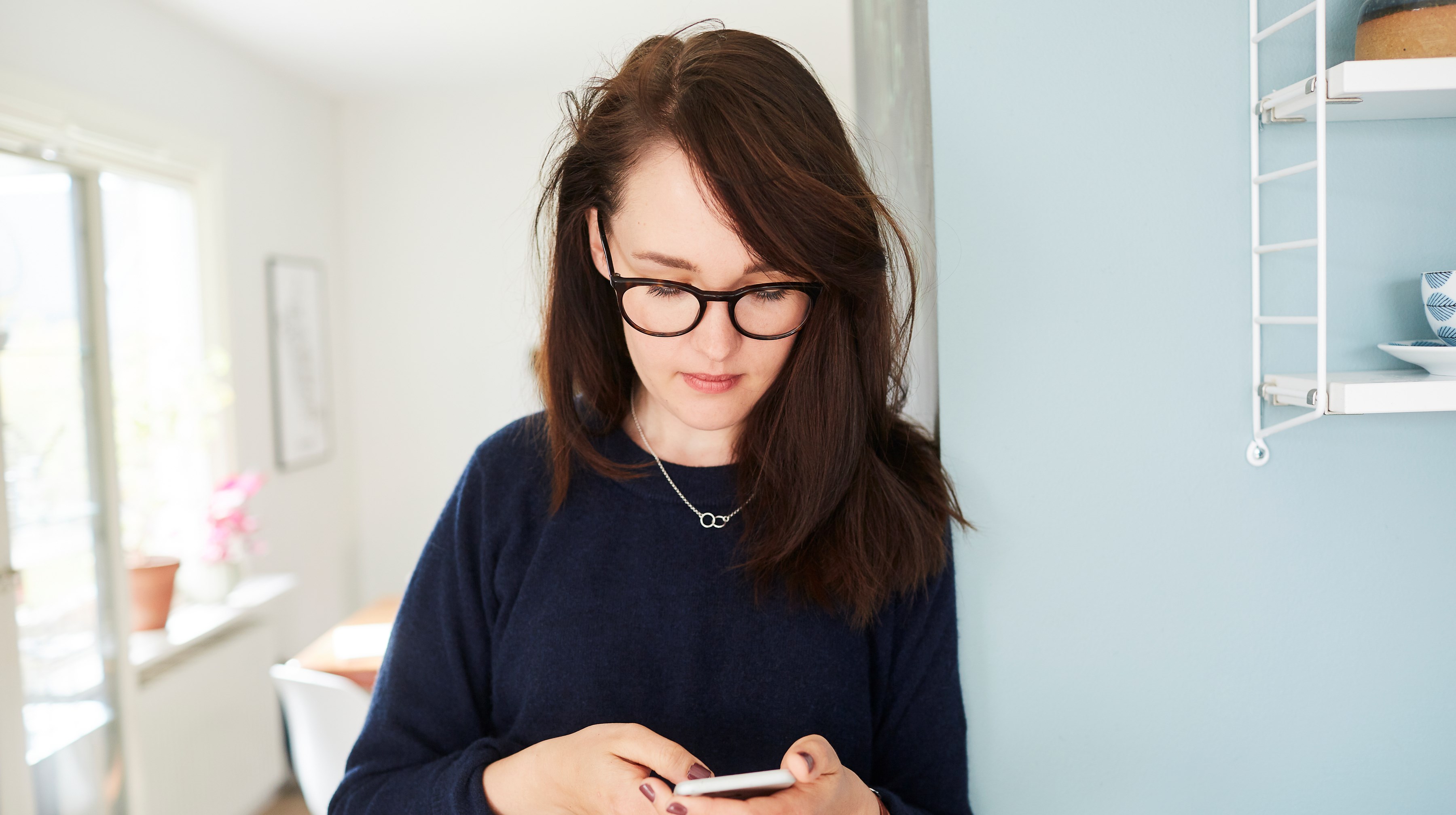 Ung kvinna med brunt längre hår sedd framifrån tittar ner på sin mobil.