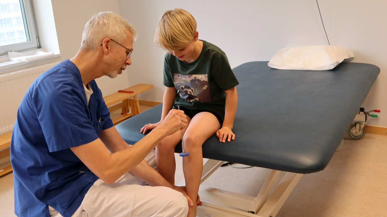 En doktor slår med en liten klubba på ett knä