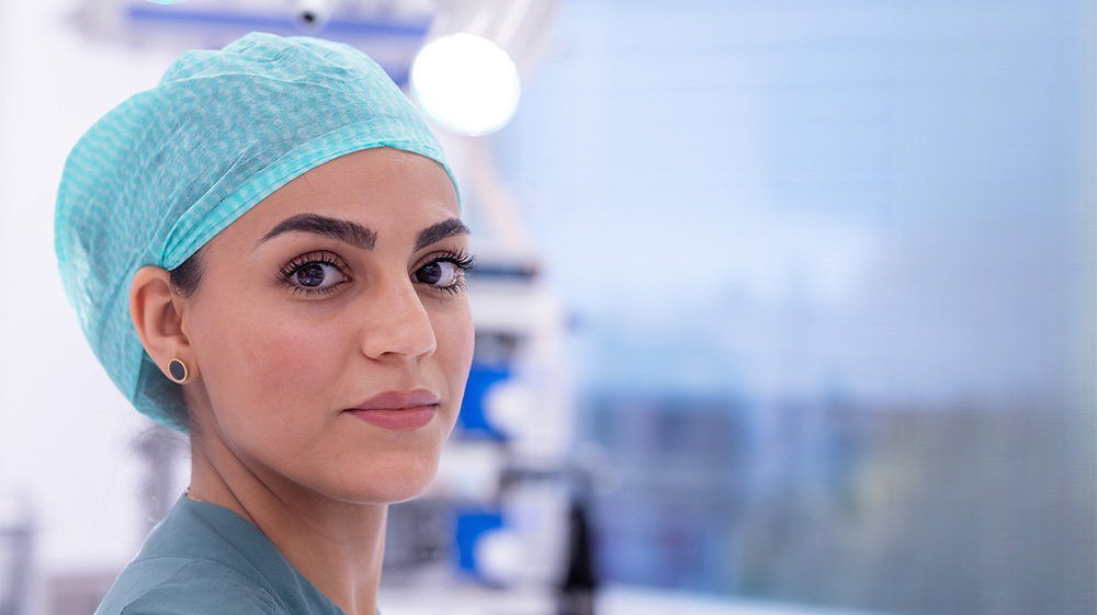 A woman wearing a medical hair net looking into the camera.