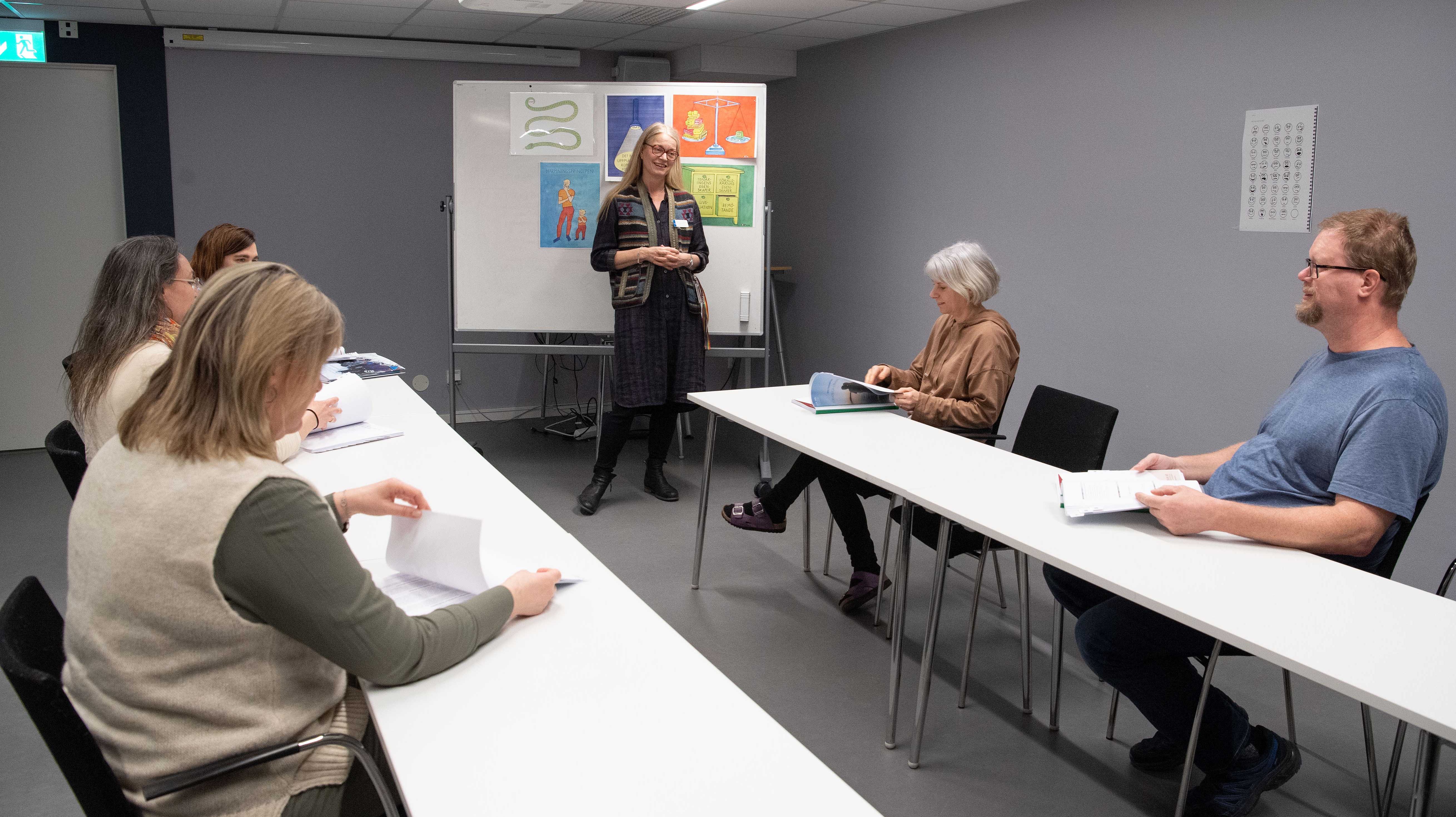En person undervisar andra personer som sitter vid två bord