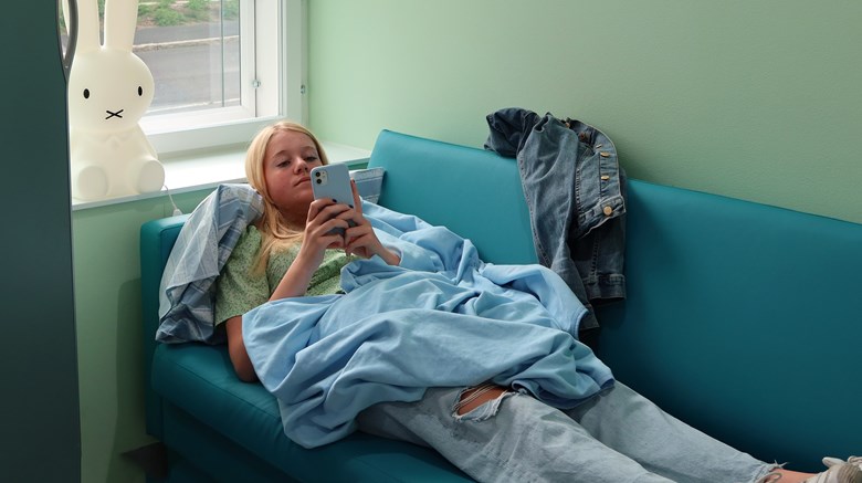 En ungdom ligger i en soffa och tittar i sin mobil.