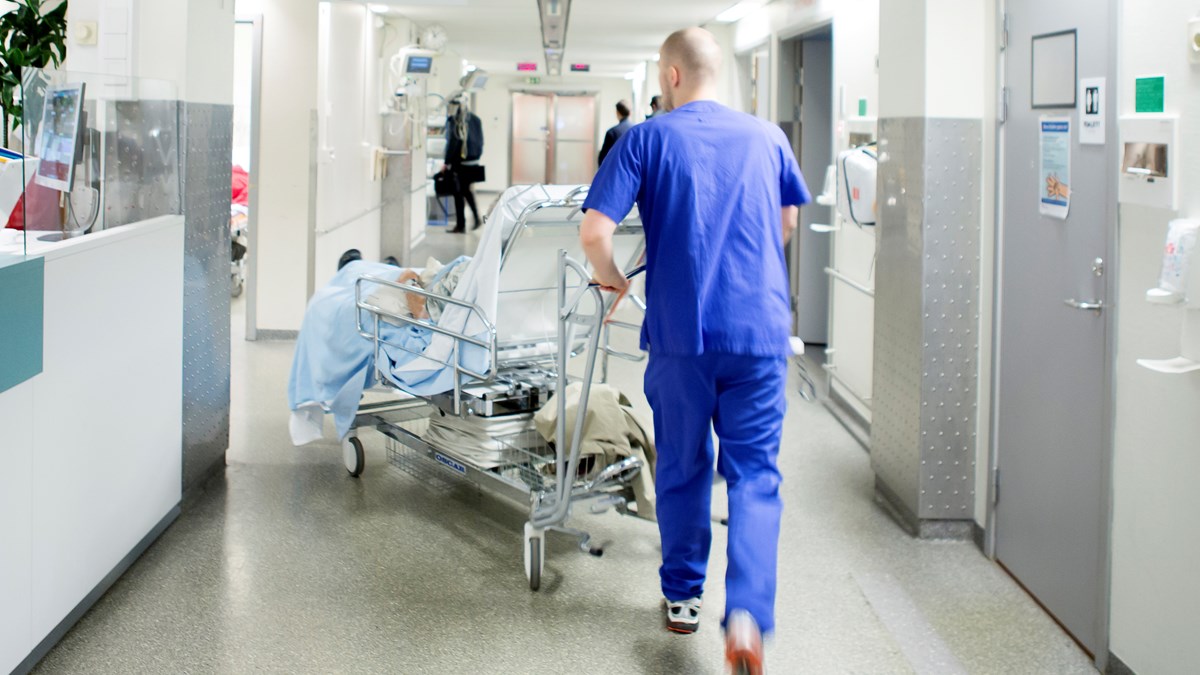 En sjukhusmedarbetare transporterar en patient i sjukhussäng i en korridor