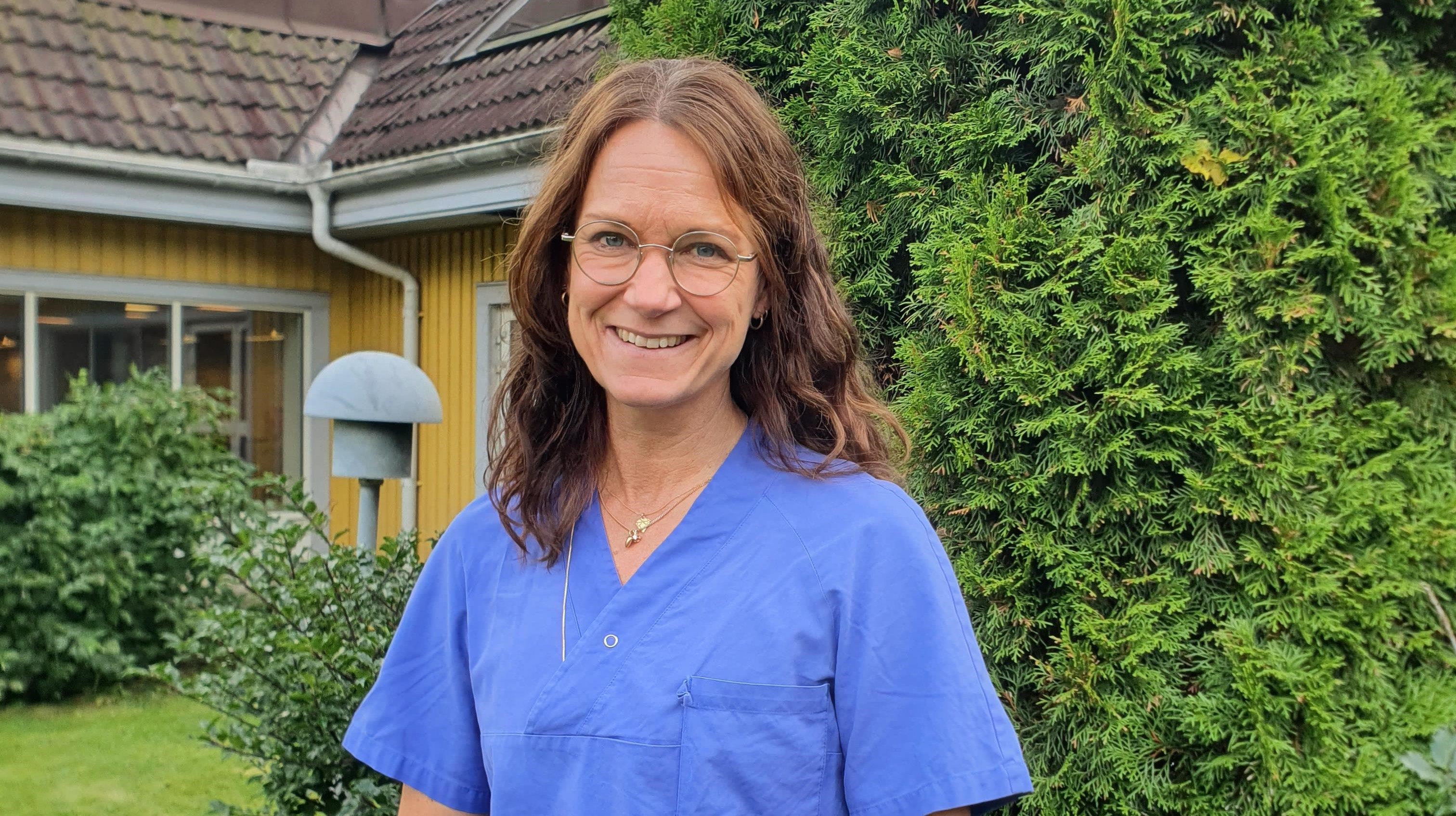 Johanna Weichbrodt iklädd blå sjukhuskläder står utomhus och ler mot kameran.
