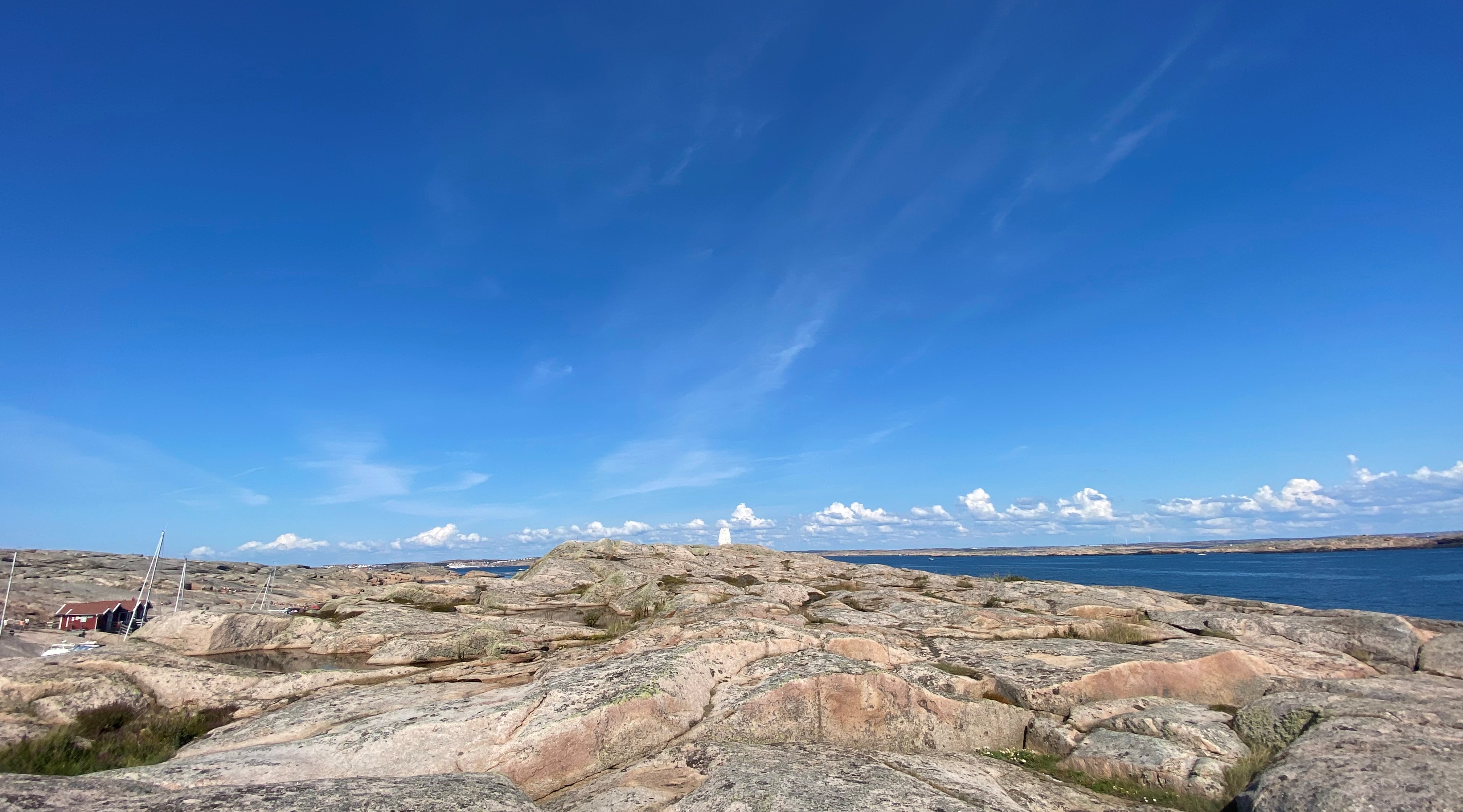 Soldränkta klippor vid havet och en klarblå himmel med några små vita molntussar.